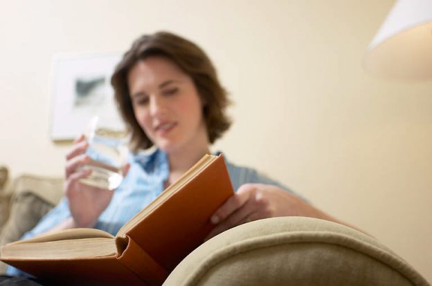 Woman reading book and drinking glass of water