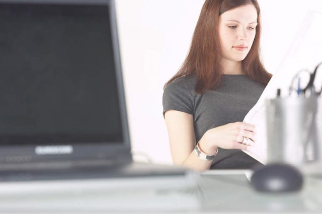 laptop on office desk, woman reads newspaper