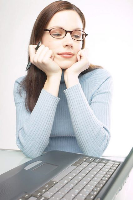 a writer stares at her computer screen with a pen in hand