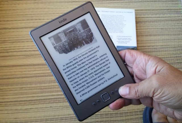 Amazon Kindle ereader in hand, books in the background