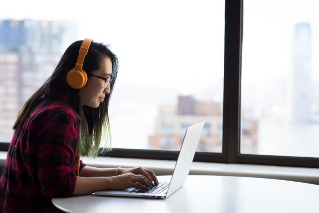 woman typing on laptop, wearing headphones. photo by Christina Morillo.