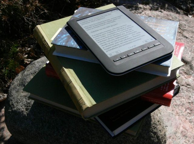 e-reader on top of paper book stack in sunshine